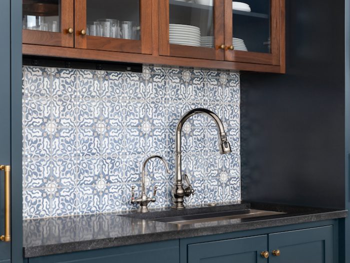 ELMHURST, IL, USA - FEBRUARY 24, 2021: A kitchen sink with a beautiful pattern tiled backsplash with a chrome faucet, black granite countertops, and surrounded by blue and wood cabinets.